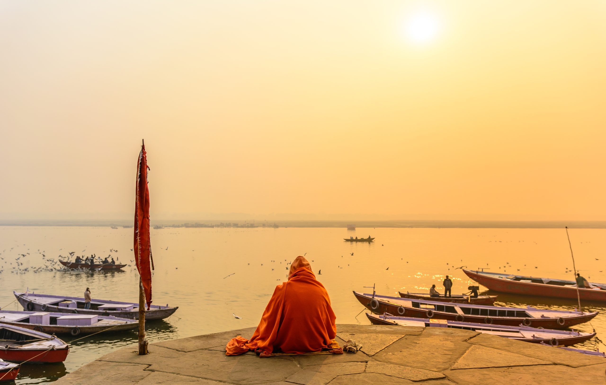 Indian sadhu in traditional saffron attire practicing yoga and meditation in morning at the bank of sacred Ganges river in Varanasi, Uttar Pradesh, India.