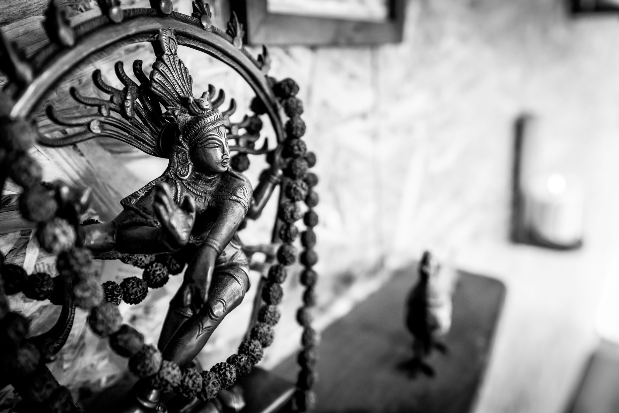Mini Shiva figure on the shelf representing origins of wellbeing in yoga center. Blank space on the background. Black and white image.